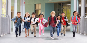 Young children with school backpacks running toward the camera with smiles on their faces