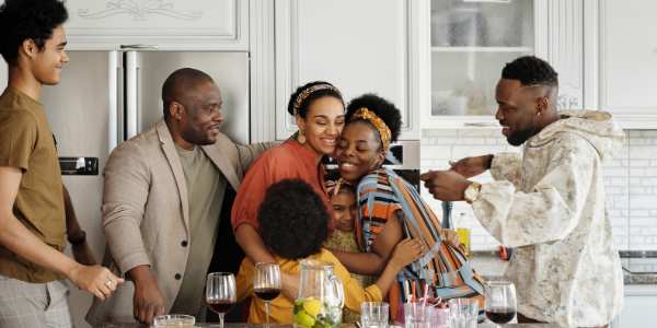 A multi-generational Black family gathers and hugs in a kitchen